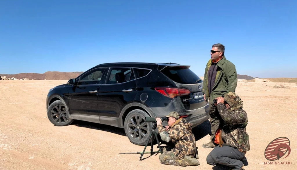 Hunters using a spotting scope and binoculars beside a black SUV on an Iranian desert plain, hunt in Iran