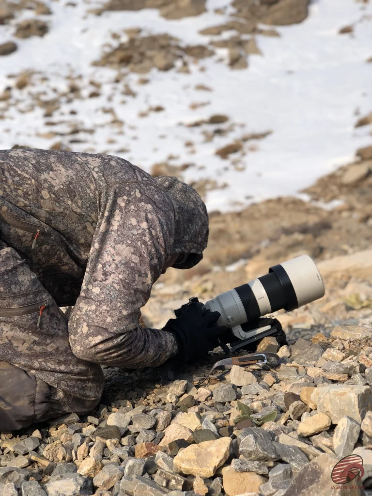 Camouflaged hunter using a telephoto camera on a snowy rocky slope in Iran, hunt in Iran