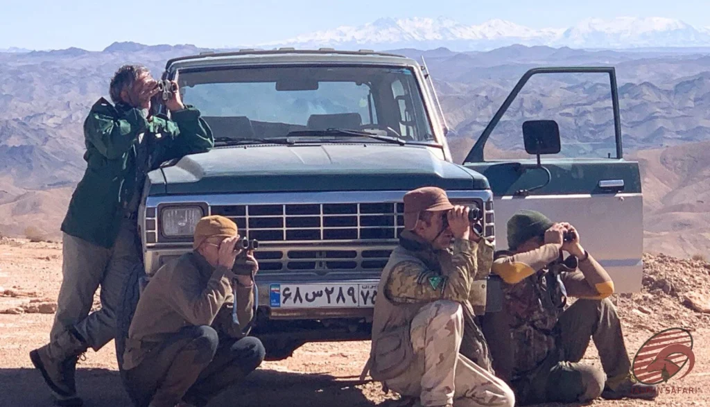 Hunters using binoculars beside a pickup with snowy peaks in Iran, hunt in Iran