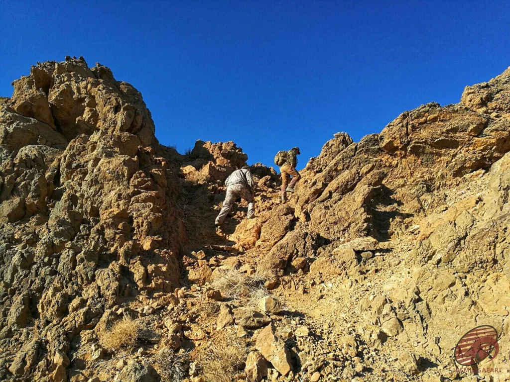 Hunters climbing a steep rocky ridge under a blue sky in Iran, hunt in Iran