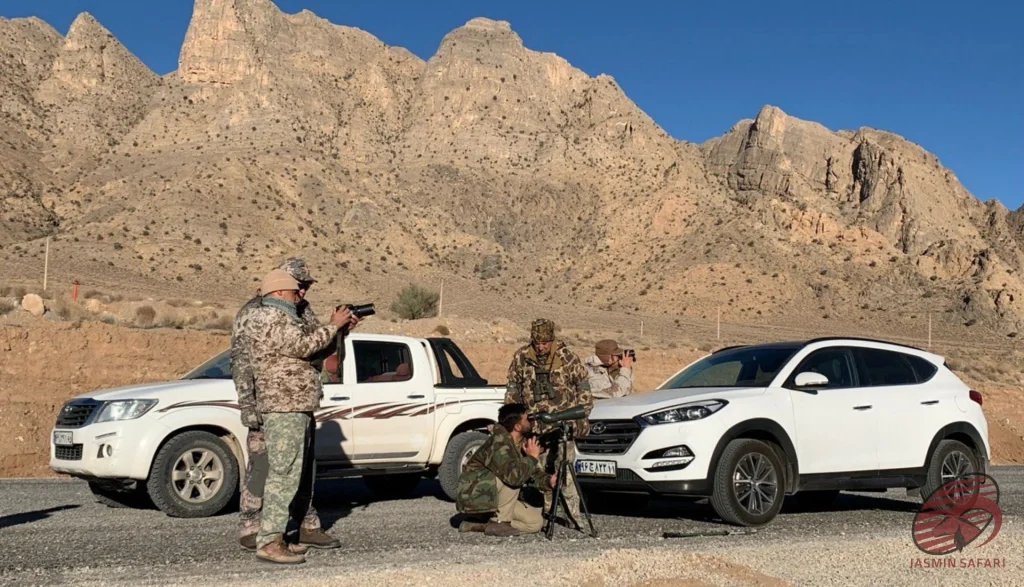 Hunters preparing with cameras and spotting scopes beside vehicles in Iran’s desert mountains,