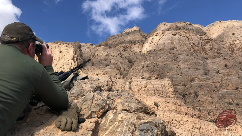 Hunter glassing limestone cliffs from a rocky ledge with a rested rifle in Iran, hunt in Iran
