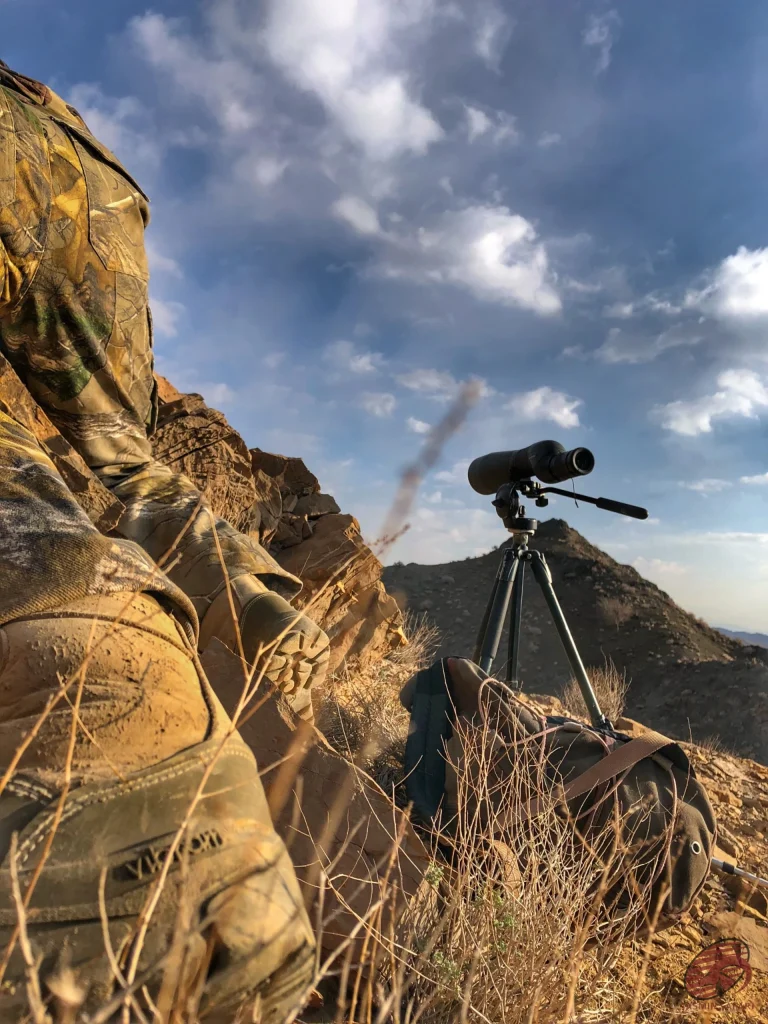 Spotting scope on a tripod on a rocky ridge with a camouflaged hunter resting in Iran, hunt in Iran