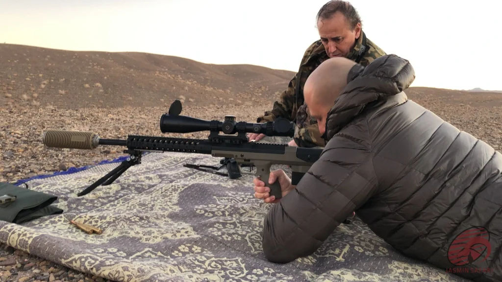 Prone hunter zeroing a precision rifle on a shooting mat in Iran’s desert hills, hunt in Iran