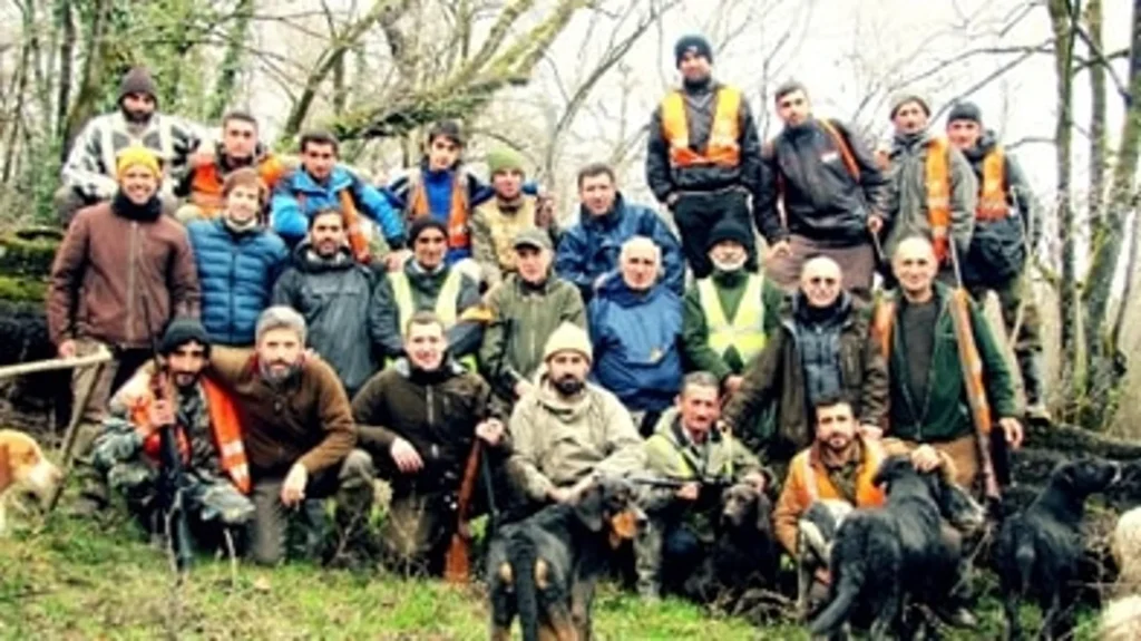 A group of hunters from different generations celebrating the tradition and camaraderie of hunting, surrounded by dogs in the forest with the keyword hunt in Iran.